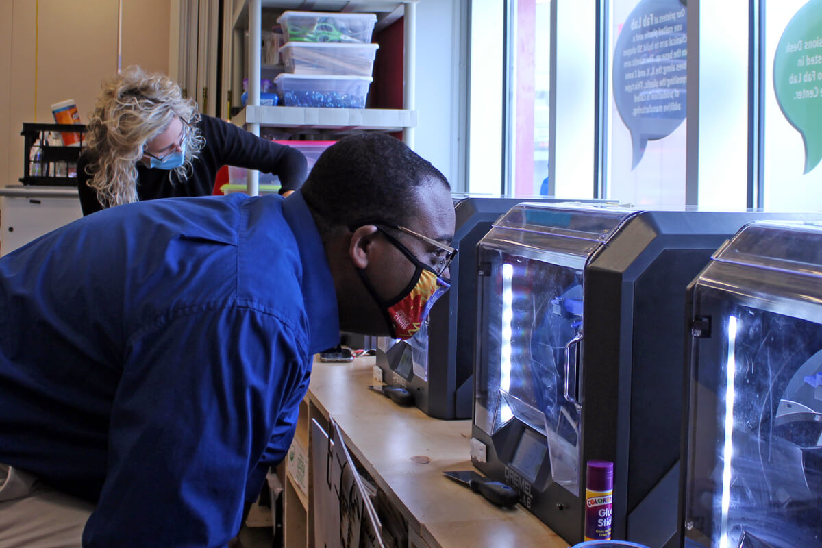 Two adults working with 3D printers